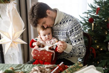 Mutlu baba ve tatlı bebek, Noel hediyelerini şık dekore edilmiş ağacın arka planında açıyorlar. Mutlu Noeller ve mutlu tatiller! Atmosferik aile zamanı.