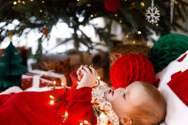 Mutlu Noeller ve mutlu tatiller! Noel ağacının altında süsleri ve ışıklarıyla şenlikli şenlikli şenlikli şamatayla oynayan tatlı bir bebek. Tatlı bebek ilk Noel kutlaması konsepti