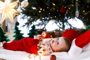 Mutlu Noeller ve mutlu tatiller! Noel ağacının altında gülümseyen ve altın ışıklar tutan neşeli bir bebek. Bebek ilk Noel kutlaması konsepti