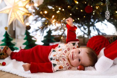 Mutlu Noeller ve mutlu tatiller! Noel ağacının altında gülümseyen ve altın ışıklar tutan neşeli bir bebek. Bebek ilk Noel kutlaması konsepti