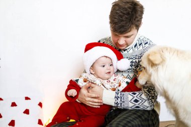 Mutlu bir baba ve Noel Baba şapkalı şirin bir çocuk şirin bir köpekle oynuyor ve Noel ağacını süslüyor. Mutlu Noeller ve mutlu tatiller! Atmosferik aile zamanı.