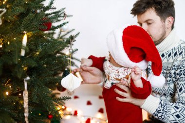 Mutlu bir baba kucağında tatlı bir çocuk ve süslü bir Noel ağacı taşıyor. Mutlu Noeller ve mutlu tatiller! Atmosferik aile zamanı, tatil hazırlığı.