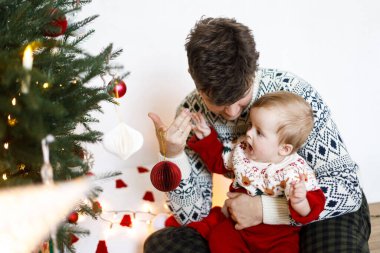 Mutlu baba kucağında tatlı bir çocuk ve süslü Noel ağacını kırmızı mücevherle süslüyor. Mutlu Noeller ve mutlu tatiller! Atmosferik aile zamanı, tatil hazırlığı.