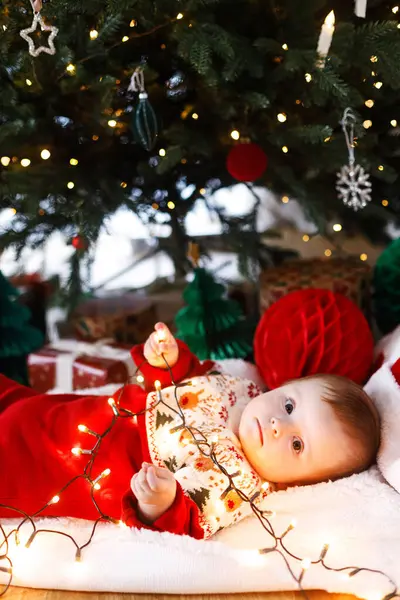 Mutlu Noeller ve mutlu tatiller! Noel ağacının altında süslerle ve hediyelerle yatarken elinde altın ışıklarla neşeli, şirin bir bebek. Bebek ilk Noel kutlaması konsepti