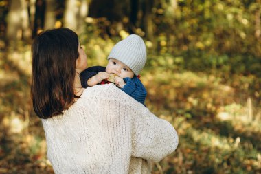Mutlu anne, sonbahar ormanında tatlı oğluna sarılıyor. Annelik. Sevimli çocuklu şık bir kadın sıcak kazaklar içinde sonbahar parkında sarılıyor ve dinleniyor.