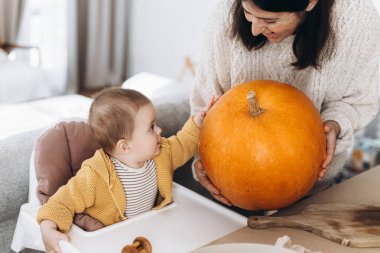 Mutlu anne ve tatlı oğlu, masasında hayaletler, örümcekler ve yarasalarla balkabağı tutuyor. Cadılar Bayramı için balkabağı oyma, balkabağı feneri yapma. Cadılar Bayramı hazırlığı