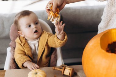 Mutlu Cadılar Bayramı. Sevimli bebek ve anne Cadılar Bayramı balkabağını ürkütücü cadılar bayramı dekoruyla masaya oyuyorlar. Aile Jack O feneri yapıyor, bayram zamanı