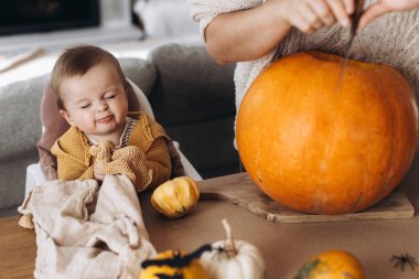 Mutlu Cadılar Bayramı. Sevimli bebek ve anne Cadılar Bayramı balkabağını ürkütücü cadılar bayramı dekoruyla masaya oyuyorlar. Aile Jack O feneri yapıyor, bayram zamanı