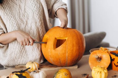 Masaya hayaletler, örümcekler ve yarasalarla balkabağı oyan mutlu bir kadın. Cadılar bayramı balkabağı kesimi, balkabağı feneri yapmak. Cadılar Bayramı hazırlığı