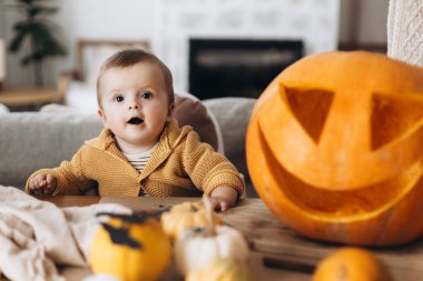 Mutlu Cadılar Bayramı. Sevimli bebek ve anne Cadılar Bayramı balkabağını ürkütücü cadılar bayramı dekoruyla masaya oyuyorlar. Aile Jack O feneri yapıyor, bayram zamanı