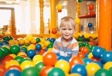 Happy boy playing at balls pool playground. School children having fun in indoor park playground. Boy playing with multi colored plastic balls in big dry paddling pool in playing centre