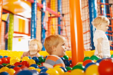 Okul çocukları kapalı alan parkında eğleniyorlar. Top havuzunda oynayan mutlu çocuk. Erkekler ve kızlar oyun merkezinde büyük kuru yüzme havuzunda çok renkli plastik toplarla oynuyorlar