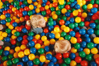 Happy kids playing in amusement park balls pool. Kids cheering and playing with plastic colourful balls. Children throwing balls high. Playing with balls: activities for children