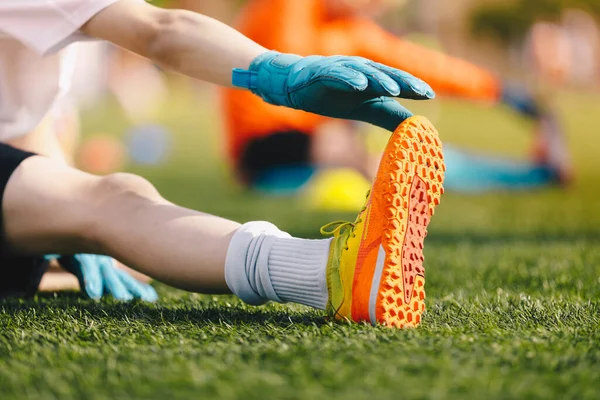 Stretches for young soccer goalies. Schoolboy at training session outdoors. Mobility exercises and stretches for goalies. Kids in football goalkeeper uniforms and cleats during warm-up training unit
