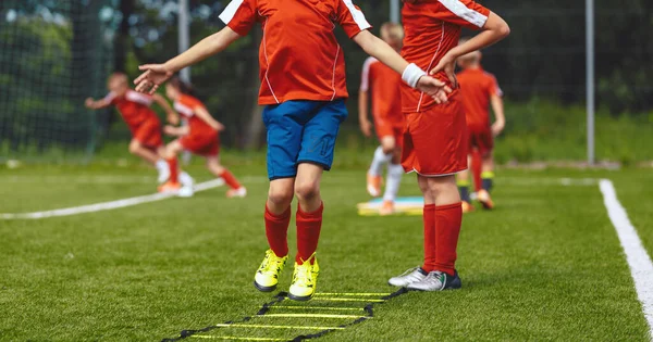 Group of children jumping over training ladder during soccer football summer camp. Boys of junior football club improving skills at a training session