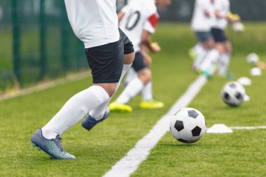 Group of soccer players kicking balls on training drill along sideline. Football training camp for youth. Footballers improving skills at training pitch