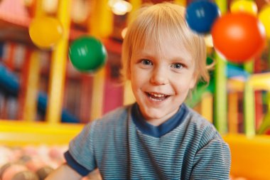 Happy little boy playing in amusement park balls pool. Child throwing balls high. Playing with balls: activities for children. Kids cheering and playing with plastic colourful balls