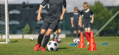 Futbol antrenmanındaki bir grup okul çocuğu. Erkekler, Slalom Eğitim Taliminde Klasik Siyah ve Beyaz Futbol Toplarını Tekmeliyor. Yaz Kampındaki Futbolcular İçin Çalışma Oturumu