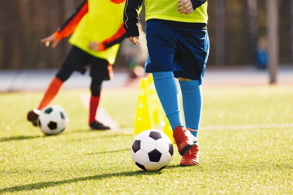 Kids in soccer winter clothing at training drill during winter practice camp. Two players kicking classic soccer balls in a slalom drill. Closeup of players legs at soccer training