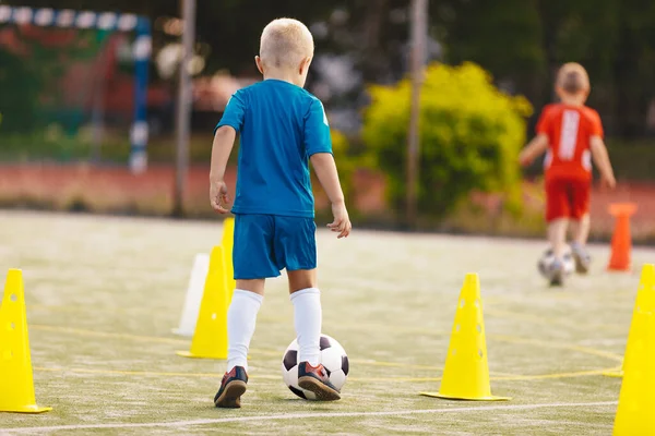 School children having fun at soccer training. Little blonde boy kicking a soccer ball at practice session dribbling drill between yellow cones. Soccer training dribbling drill for youth.