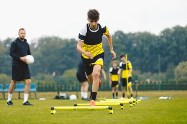 Engellerin üzerinden atlayan genç sporcu çocuk. Gençler Futbol Kulübü için açık hava futbol antrenman birimi. Yaz Kampı 'nda Antrenman Oyuncuları