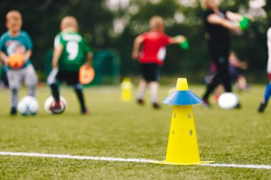 Küçük çocuklar koçla futbol antrenmanında eğleniyorlar. Futbol kampında çocuklarla oynayan antrenör. Futbol sarı eğitim konisi ve arka planda bulanık oyuncular 
