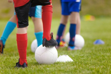 Çocuklar için futbol antrenmanı. Futbol dersine katılan futbolcuların bacakları. Çocuklar dışarıda spor yapıyor. Futbol kramponlu okul çocukları klasik futbol toplarını tekmeliyor.
