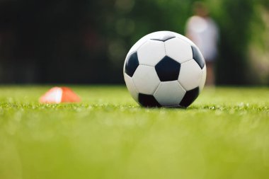 Futbol topu ve antrenman sahasında kırmızı koni işareti. Futbol sahasında. Bulanık Arkaplan 'daki futbol stadyumu. Arka planda Çalışan Genç Oyuncular
