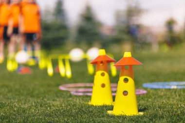 Spor eğitim aletleri. Futbol ekipmanları sahada. Spor sahasında sarı ve kırmızı tatbikat konileri. Spor eğitiminde arka plandaki çocuklar