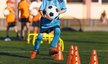 Gençlik Spor Eğitimi. Beden eğitimi dersinde futbol antrenmanı. Spor Eğitiminde Çocuklar Ellerindeki Futbol Toplarını Tutuyor ve Eğitim Konileri Arasında Hızlı Koşuyorlar
