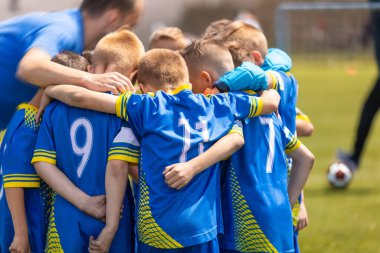 Futbol takımı mola sırasında bir koçla bir çember içinde toplanır. Futbol takımındaki çocuklar birlik olup koçun motivasyon konuşmasını dinliyorlar. Mavi futbol formalı çocuklar.