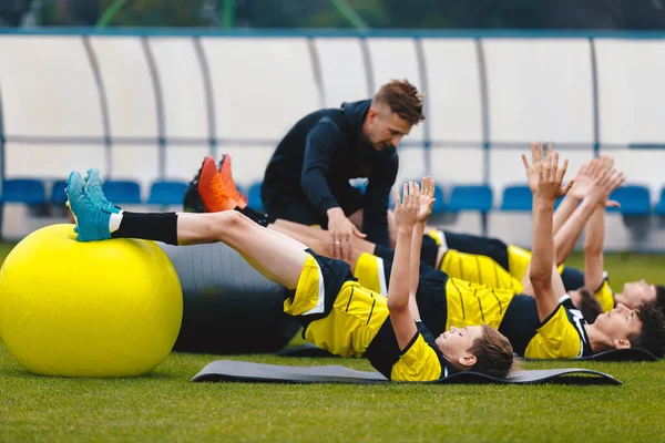 Group of Football Players on Physiotherapy Training. Young Trainer Giving Advice to Player on Agility Training and Stretching. Coaching Soccer in Teenage Football Team. Young Soccer Players