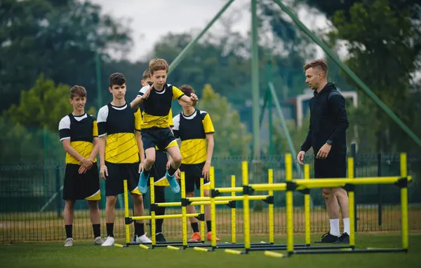 Teenagers on soccer training camp. Boys in football practice with a young coach. Junior-level athletes jump over hurdles and improve strength and coordination skills. Soccer pre-season summer camp