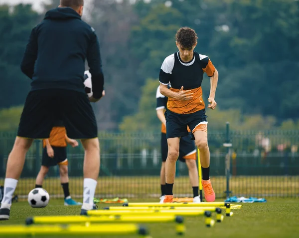 Boys' Soccer Practice Camp. Teenage boys in football training with a young coach. Teenagers on football camp. Junior-level athletes jump over hurdles. Soccer strength and coordination skills