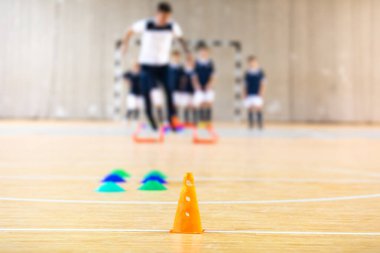 Kapalı futbol antrenmanı sırasında çocuklara koçluk yapan genç bir koç. Futsal eğitim tatbikatları. Kapalı alanda futbol ekipmanları. Beden eğitimi dersi sırasında okul çocukları. Beden eğitimi eğitim ekipmanları araçları