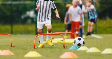 Koçla beden eğitimi eğitimi alan küçük çocuklar. Spor yapan çocuklar antrenman sahasında engellerin üzerinden atlıyorlar. İlkokul yaşı için spor okulu eğitimi. 