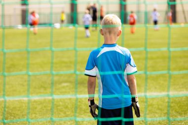 Kaleci Üniformalı ve Eldivenli Küçük Çocuk Bir Futbol Gol Alıyor. Çocuklar okul spor sahasında futbol oynuyorlar.