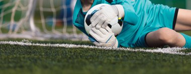 Futbol kalecisi bir futbol topunu göğsüne sıkı tutuyor. Genç kaleciler için futbol eğitimi 