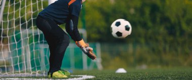 Eldivenli futbol kalecisi ve hareket halinde bir futbol topu. Genç kaleciler için futbol eğitimi 