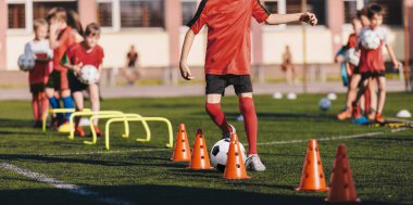 Okul sahasında futbol antrenmanına katılan çocuklar. Çocuklar için futbol antrenmanı. Beden eğitimi sınıfında çocuklara koçluk yapan genç bir adam.