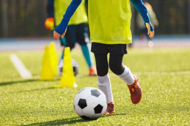Kış güneşli gününde Futbol Eğitiminde Okul Çocukları. Futbolcular, antrenman konisiyle top sürerken top atıyorlar. Sonbahar Futbol Antrenman Birimi