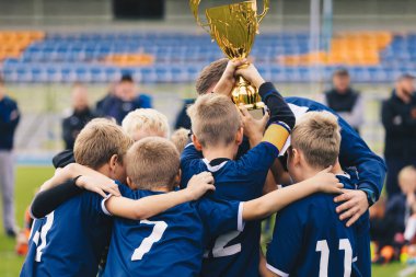 Mavi Futbol Üniformalı Genç Çocuklar Altın Kupa 'da Yükseliyor. Futbol takımındaki Mutlu Çocuklar Okul Turnuvasında Altın Kupa kazanıyor. Genç Koç, Çocuk Futbolcularla Başarıyı Kutluyor