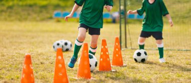 Futbol antrenman kampındaki çocuklar. Genç oyuncular antrenman konilerinin arasına top sürüyor. Futbol yaz kampı. Futbol antrenmanındaki oyuncular