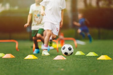 Genç çocuk antrenman engelli parkurunda futbol topuyla koşuyor. Spor eğitimi alan bir grup okul çocuğu. Çocuklar yaz günü futbol antrenmanı yapıyor.