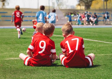 Genç Futbol Akademisi Oyuncuları. Mutlu Çocuklar Dışarıda Spor Yapıyor. Üç Erkek Spor Dostu Futbol Sahasında Oturuyor Sideline ve Futbol Maçı İzliyor. Futbol formalı okul çocukları.