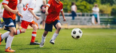 Gençler futbol ligi sırasında futbol oynarlar. Hız düellosu oyuncuları. Çocuklar spor maçında eğleniyor. Futbolcular çimlerin üzerinde topa vuruyor. Kırmızı beyaz futbol formalı çocuklar.