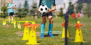 Okul çocukları için futbol kampı. Çocuklar dışarıda futbol antrenmanı yapıyor. Engel parkurunda koşan çocuklar