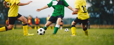 Gençler Futbol Maçı. Bir grup erkek birlikte futbol oynuyor. İki Futbol Takımındaki Okul Çocukları Turnuva Maçı sırasında Top Tekmeliyor. Sarı ve Yeşil Futbol tişörtlü Genç Sporcular