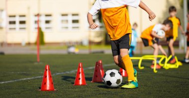 Antrenman talim topundaki futbolcu çocuk. Futbol topu ve sahanın üzerindeki direkler. Genç Futbolcu Eğitimi. Külahlarla Top Eğitimli Genç Futbolcu