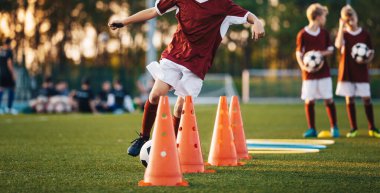 Kestane rengi formalı genç futbolcular gün batımındaki antrenman sırasında yeşil bir alanda külahta salya akıtıyorlar.
